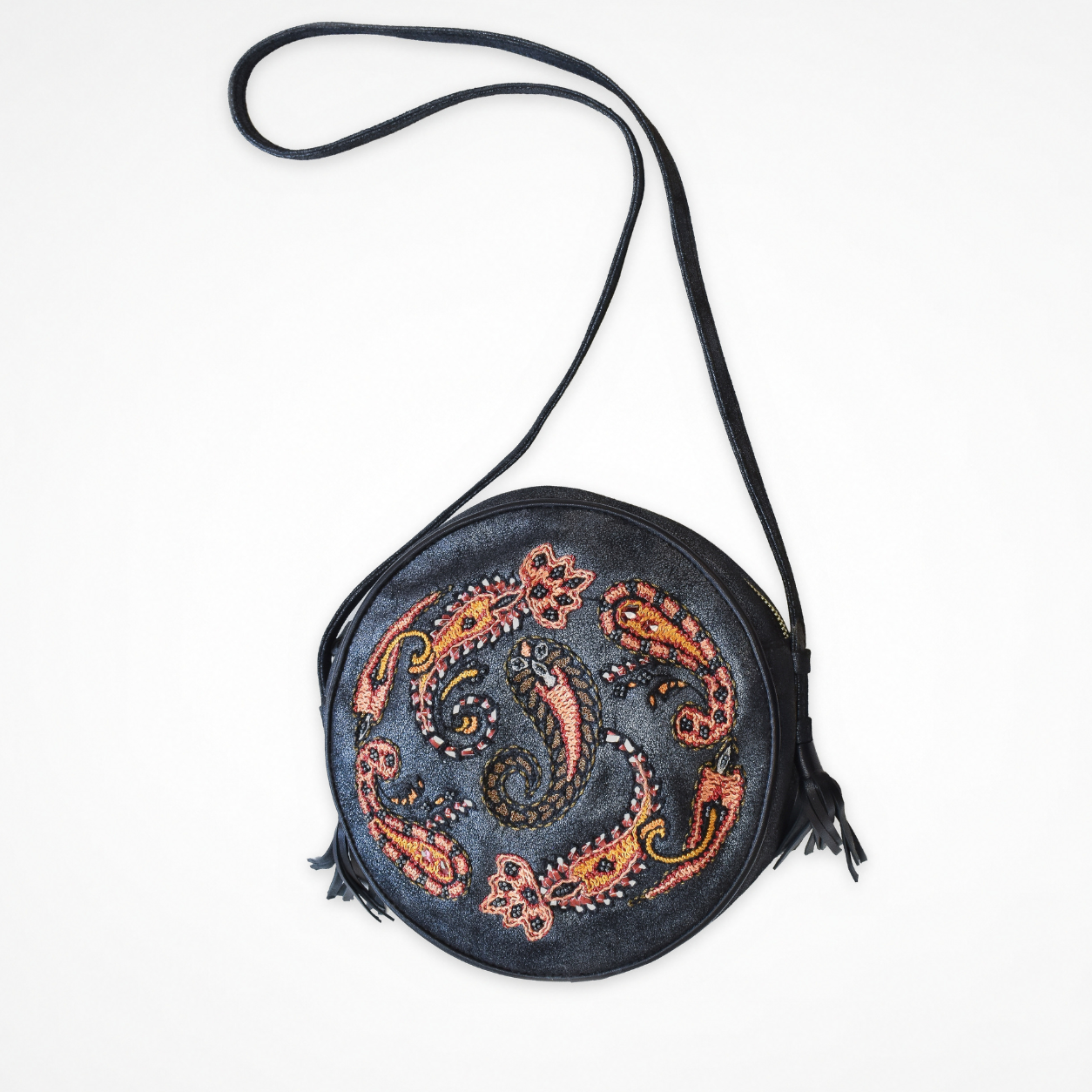 Shiny black round crossbody bag with embroidered paisley motifs, long shoulder strap and tassel details