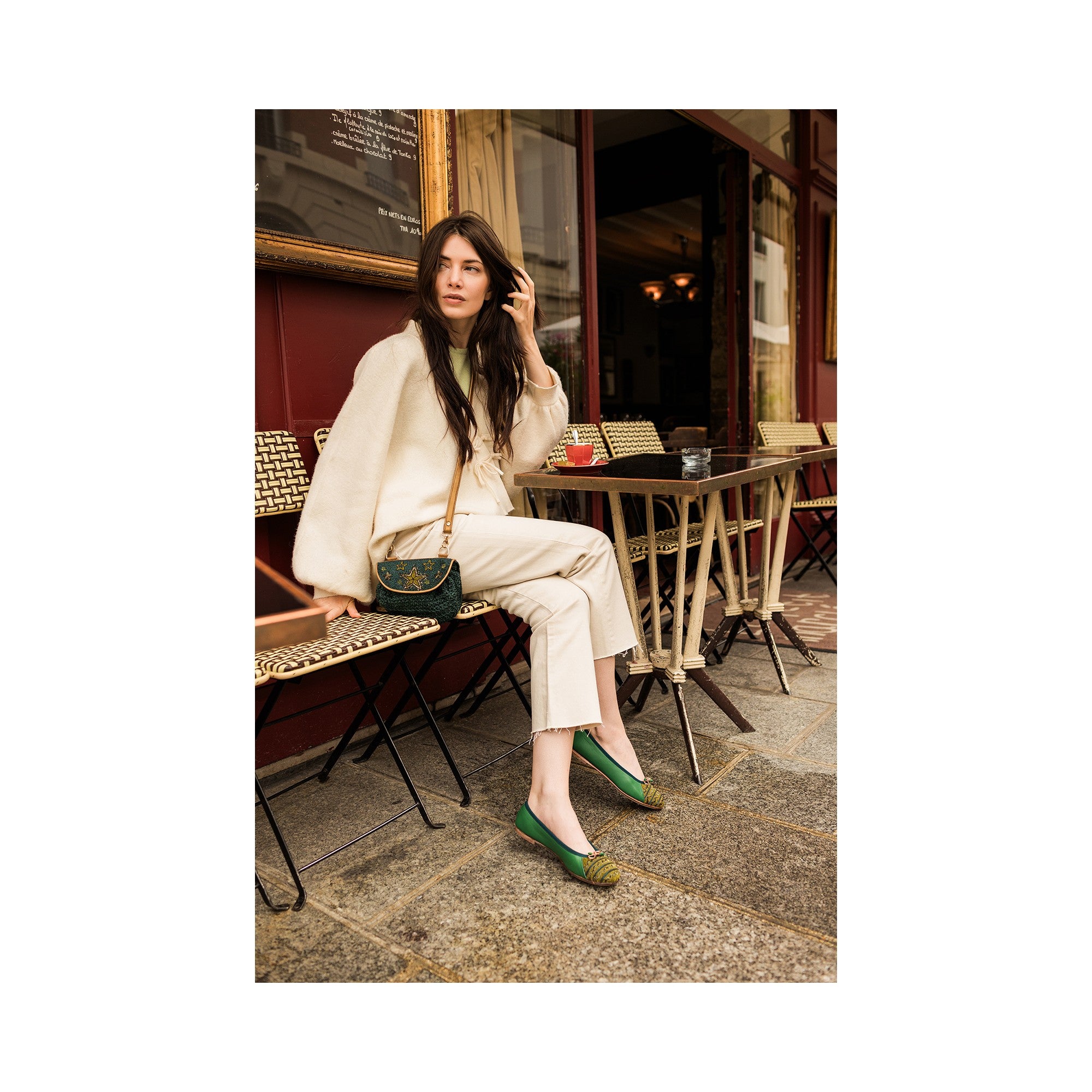 Woman wearing a dark green crochet Starry Night Accordion crossbody bag with gold embroidered stars at a café